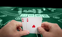 two hands holding poker cards in front of a casino table game